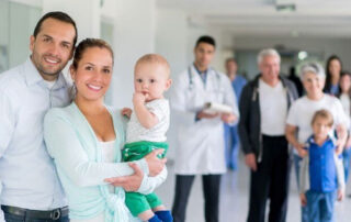 A young couple holding a baby in a hospital corridor with hospital staff standing behind them.