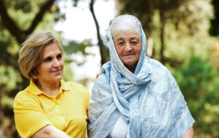 A woman in a yellow tshirt walking with an older woman wearing a shawl over her head and shoulders.