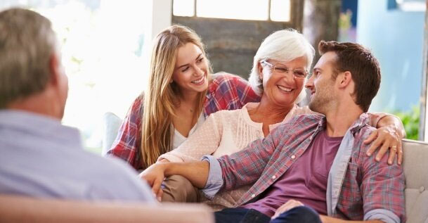 CHPCA-NEWS-National-Framework-on-Advance-Care-Planning-Aims-to-Ensure-Canadian’s-Voices-are-Heard An elderly woman with white hair sitting on a couch with her arm around a younger male. A young female sits on the other side of her looking at her and smiling.
