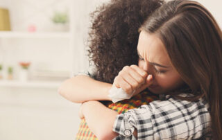 A couple hugging, the woman is holding a tissue in her hand and is looking down with her eyes closed.