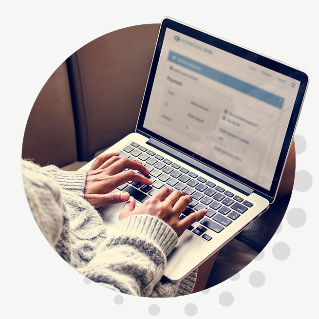 A closeup of a woman in a sweater typing on a laptop.