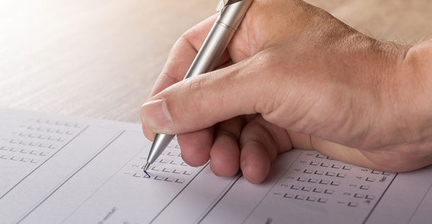 A close up of a hand holding a pen writing a checkmark in a box on a piece of paper.